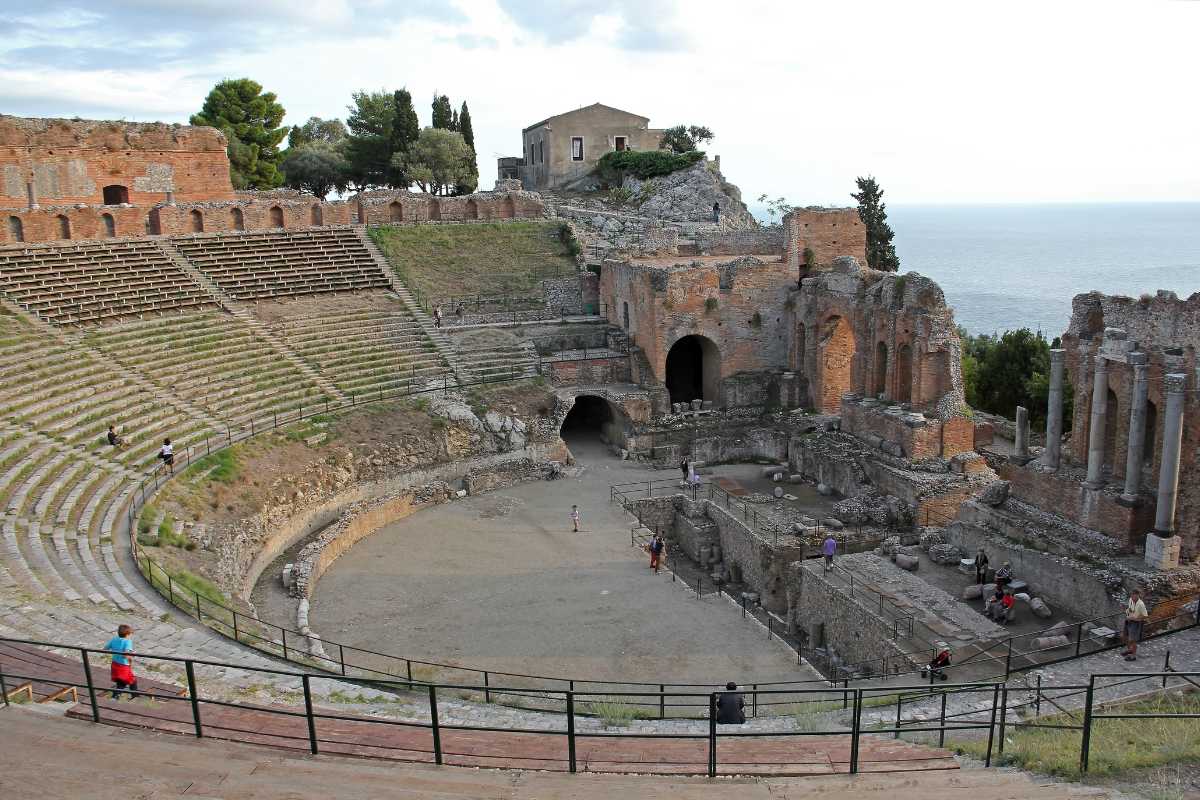 Vista panoramica del Teatro Antico e della costa di Taormina con l’Etna sullo sfondo, luce calda al tramonto