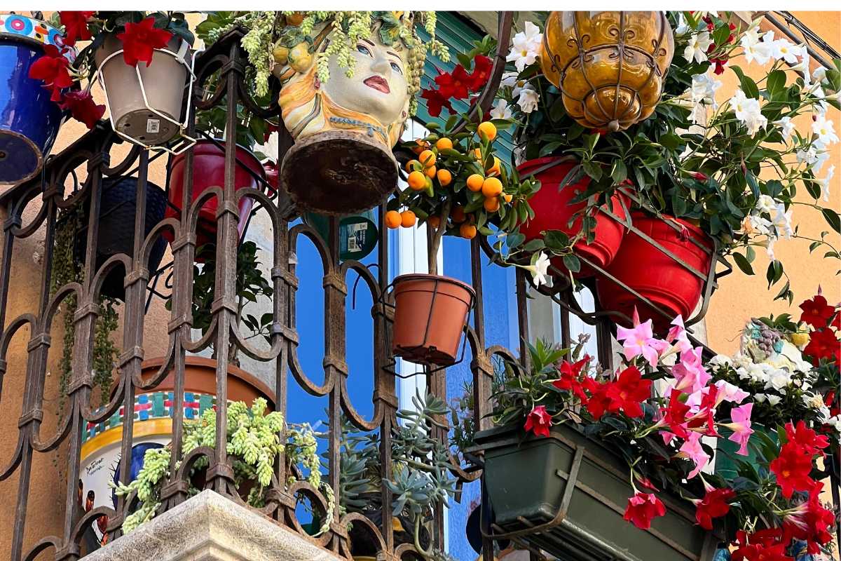 Veduta di una tavola imbandita con piatti tipici siciliani e Taormina sullo sfondo, atmosfera conviviale all’aperto