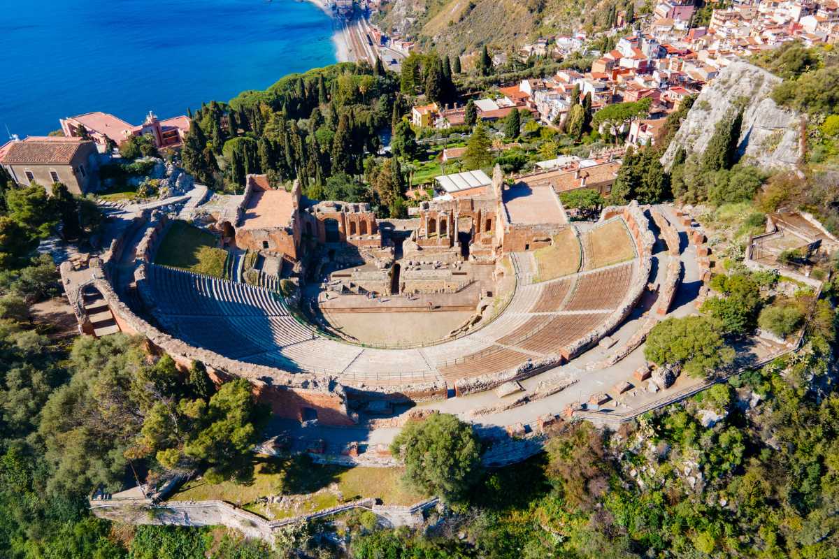 Panoramica di una famiglia con bambini che gioca sulla spiaggia sabbiosa di Isola Bella, Taormina, con mare calmo e ombrelloni colorati, atmosfera felice e rilassata